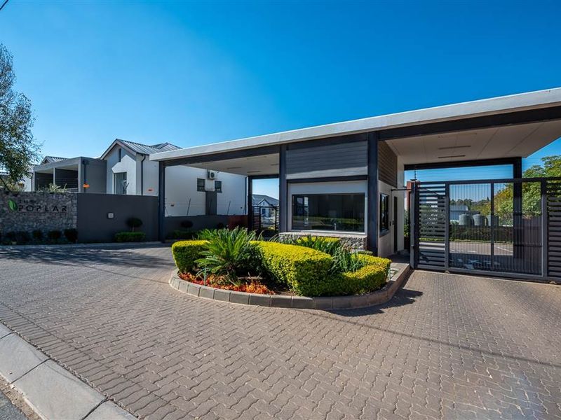 The secure entrance to The Poplar apartment complex, featuring a modern guard house, automated security gate, and well-maintained paved driveway and landscaping.