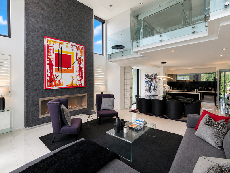 Spacious open-plan living area featuring a double-volume ceiling, modern built-in fireplace, and a mezzanine level with glass balustrades.