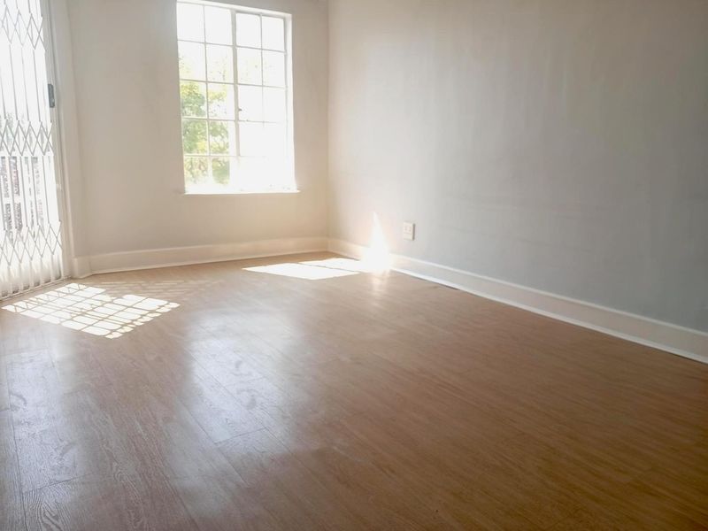 A bright, empty bedroom featuring light-toned laminate flooring, neutral walls, and a security gate leading to an outdoor area.