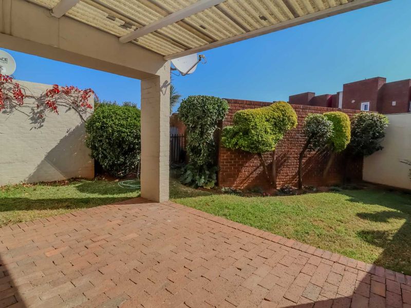 A private outdoor patio area featuring brick paving, a covered roof structure, and a small garden space enclosed by brick boundary walls.
