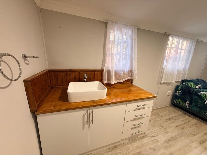 Bedroom featuring a built-in vanity area with a vessel sink, wooden countertop, and white cabinetry, complemented by laminate flooring and timber wall paneling.
