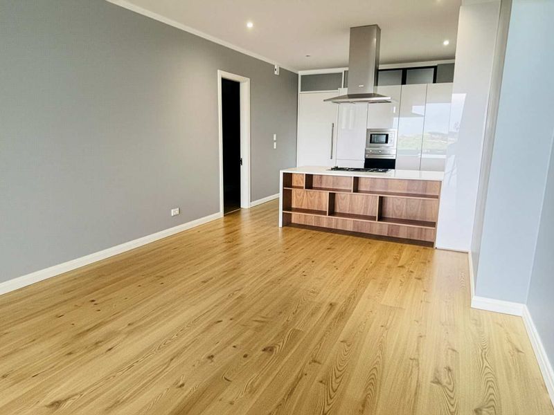 Modern open-plan living area featuring light wood flooring, recessed lighting, and a sleek kitchen island with built-in appliances and high-gloss cabinetry.