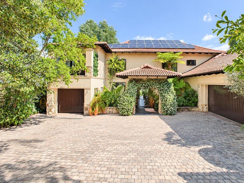 A well-maintained front elevation featuring a paved driveway, double garage, and solar panels installed on the tiled roof.