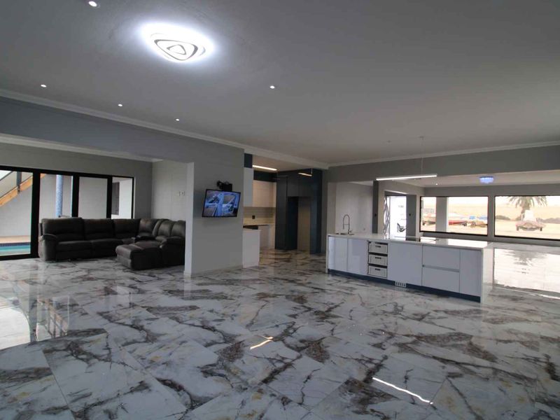 Spacious open-plan living area featuring high-end marble-look flooring, a modern kitchen island, and large sliding doors providing seamless indoor-outdoor flow.