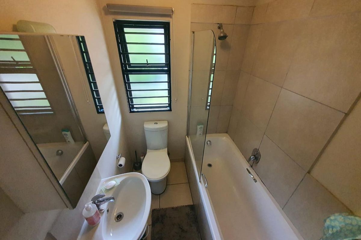 A functional bathroom featuring a bathtub with a glass shower screen, a pedestal basin, and a toilet, finished with neutral wall tiling.