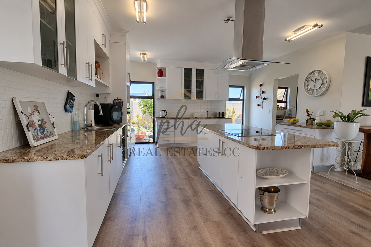 Modern kitchen featuring white cabinetry, granite countertops, a central island with an integrated cooktop, and a stainless steel extractor fan.