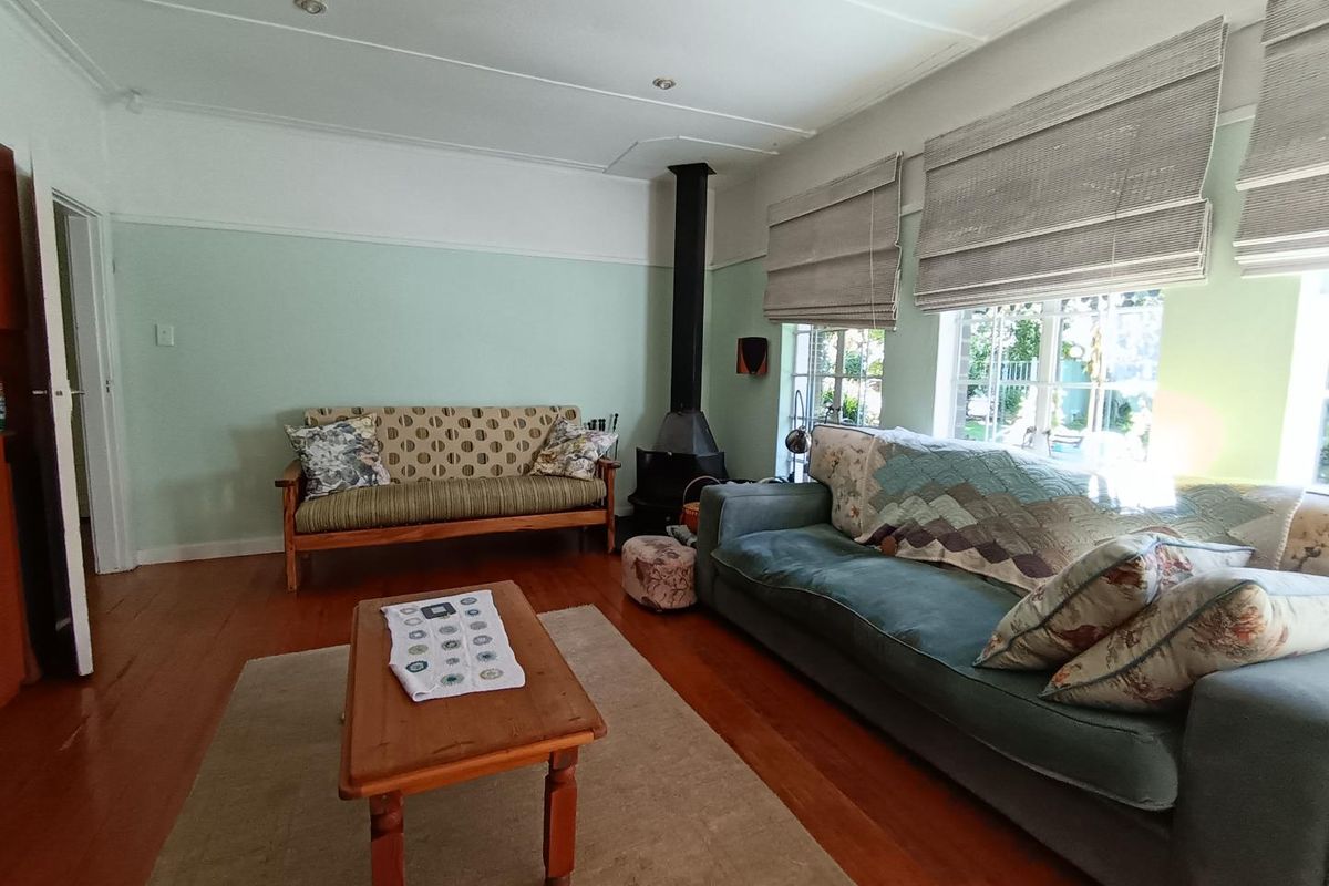 A cozy living room featuring polished timber flooring, a built-in wood-burning fireplace, and large windows with fitted blinds.