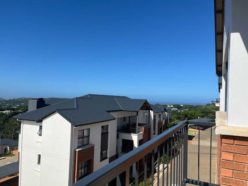 A balcony with a metal balustrade offering an elevated view of the surrounding apartment complex and landscape.