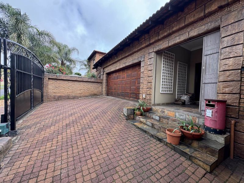 Front exterior view featuring a paved driveway, double garage, stone-clad facade, and secure gated entrance.
