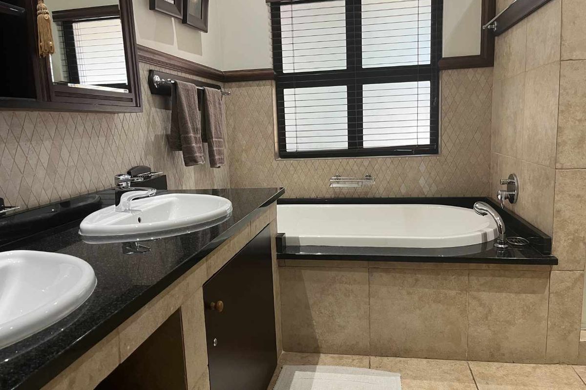 A well-maintained bathroom featuring a double vanity with granite countertops, a built-in bathtub, and neutral wall and floor tiling.