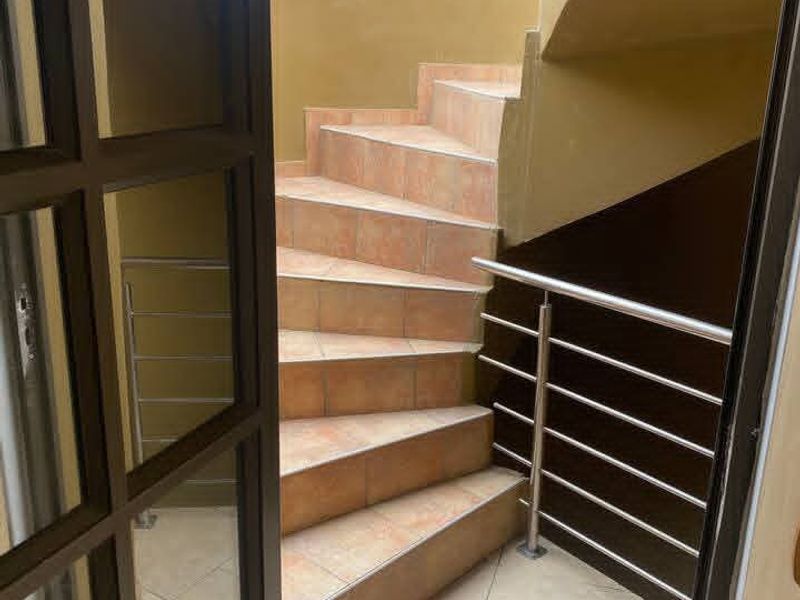 A tiled staircase featuring a stainless steel handrail, viewed through a glass-paned door in a well-maintained hallway area.