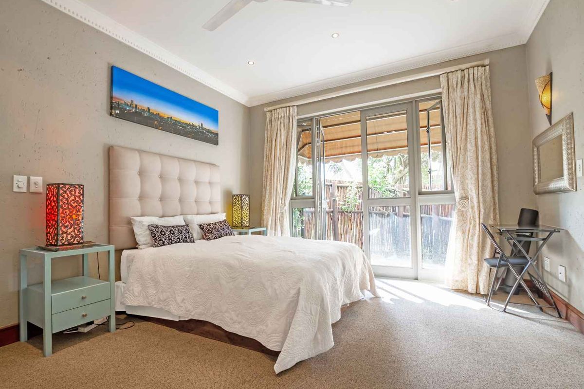 A well-lit bedroom featuring neutral walls, carpeted flooring, and large glass sliding doors that provide direct access to an outdoor patio area.