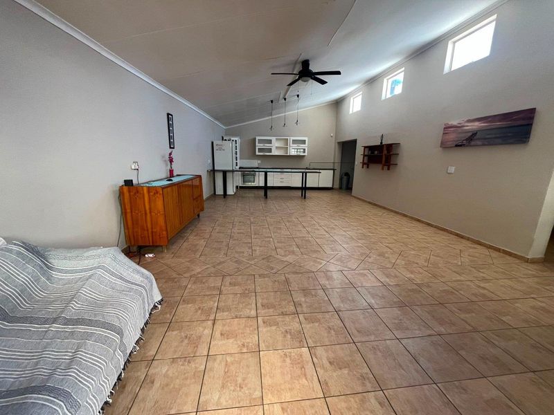 Spacious open-plan living area featuring tiled flooring, a vaulted ceiling with a fan, and a functional kitchen space with built-in cabinetry.