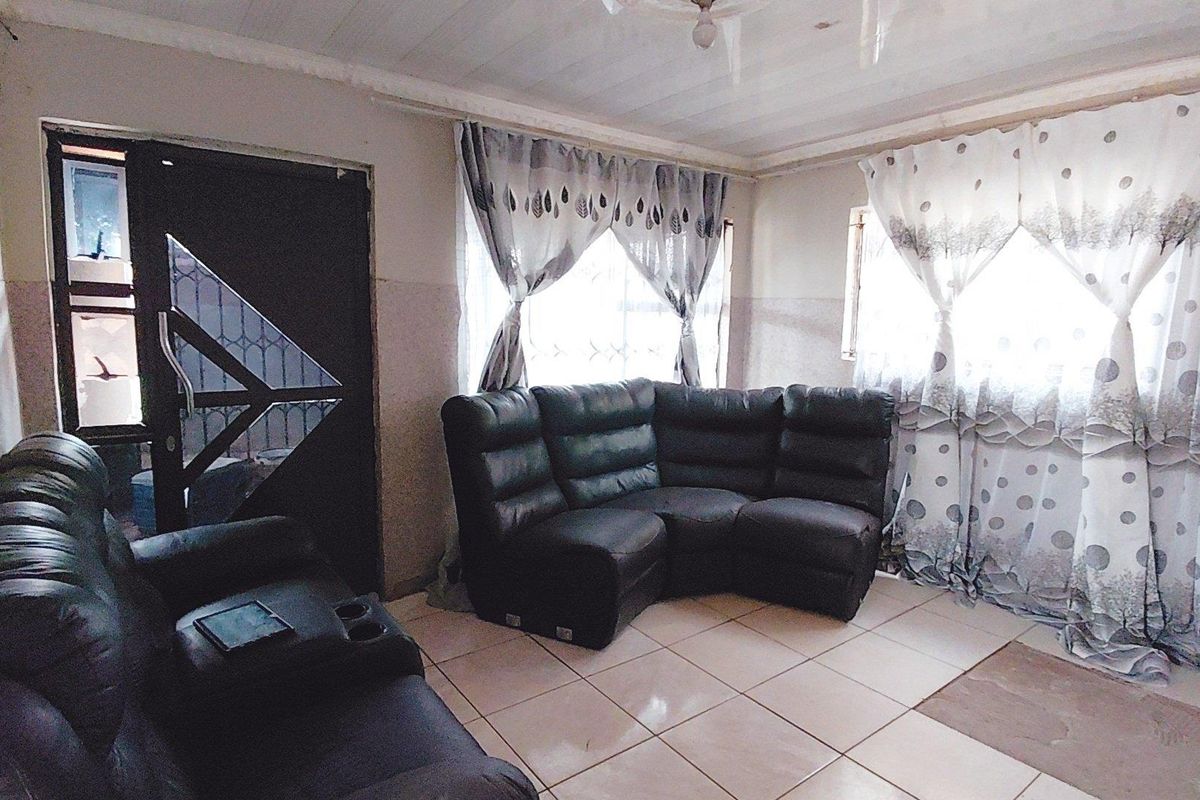 A living room featuring tiled flooring, a timber ceiling, and a security gate entrance, offering a functional space with potential for cosmetic updates.