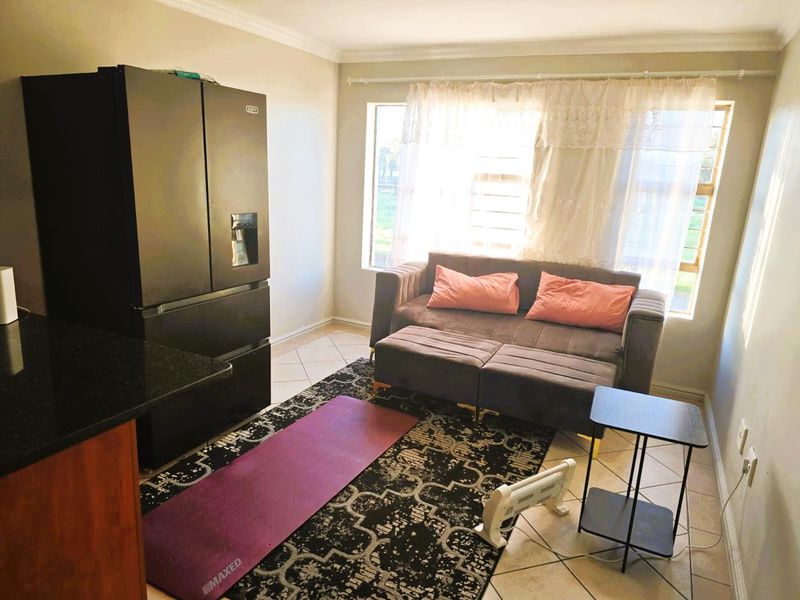 Open plan living area featuring tiled flooring, cornicing, and large windows with security bars, providing a functional and bright space.