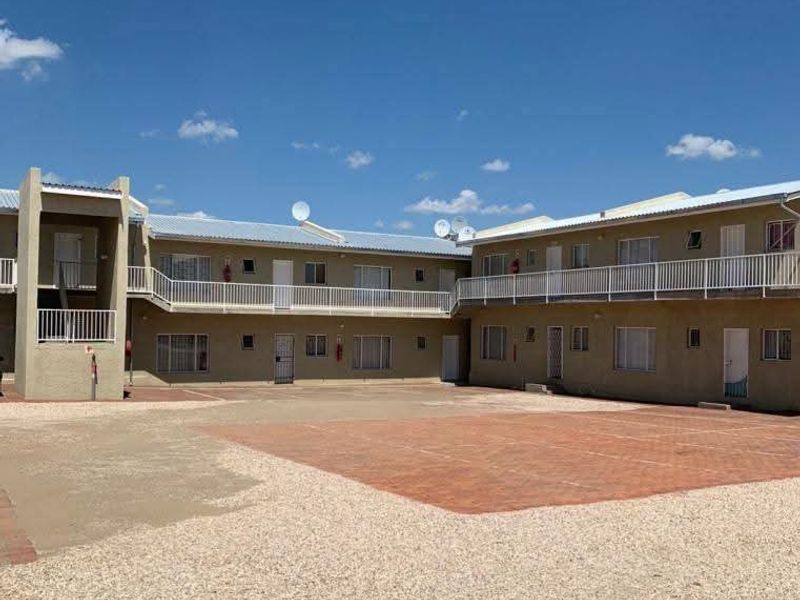 Exterior view of a multi-unit townhouse complex featuring a shared paved courtyard, gravel driveway, and upper-level balcony access.