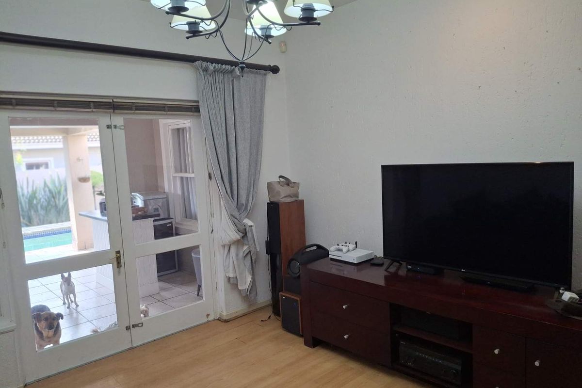 A living room featuring laminate flooring and a double glass door providing access to the outdoor patio area.