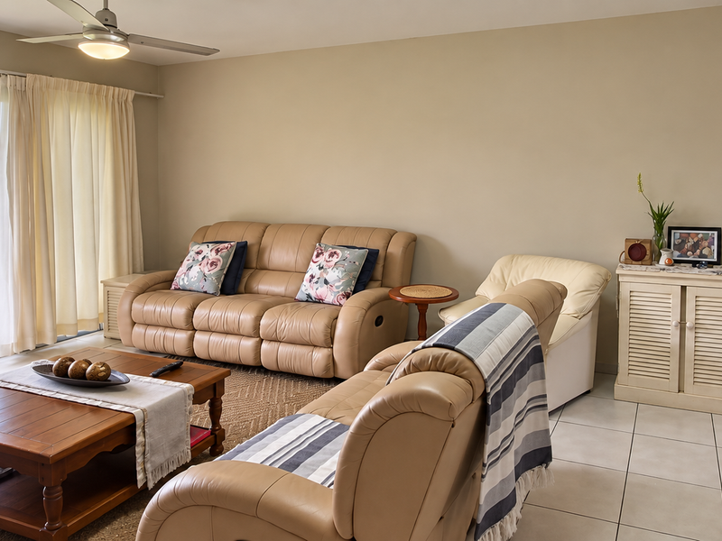 Spacious living room featuring tiled flooring, a ceiling fan, and large sliding glass doors that open onto a private patio and garden area.