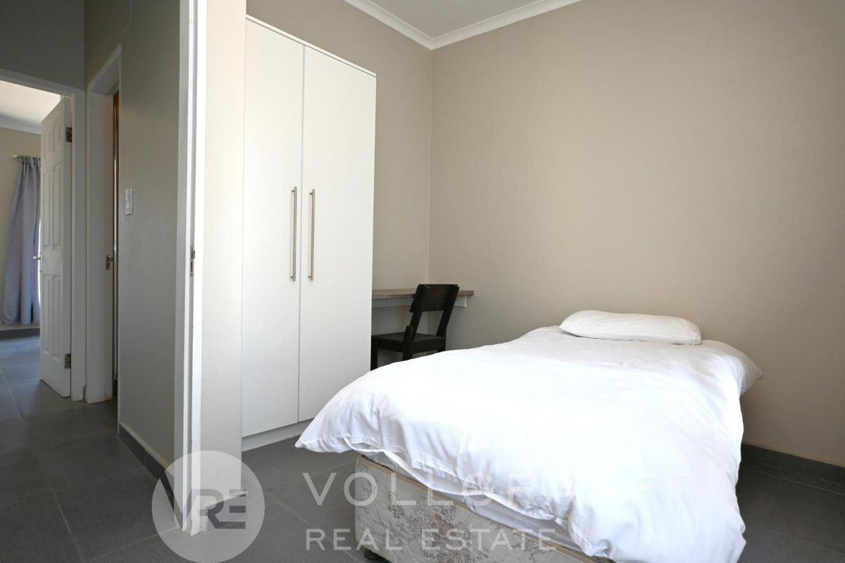 A clean bedroom featuring neutral wall tones, tiled flooring, and a built-in wardrobe, offering a functional and well-maintained living space.