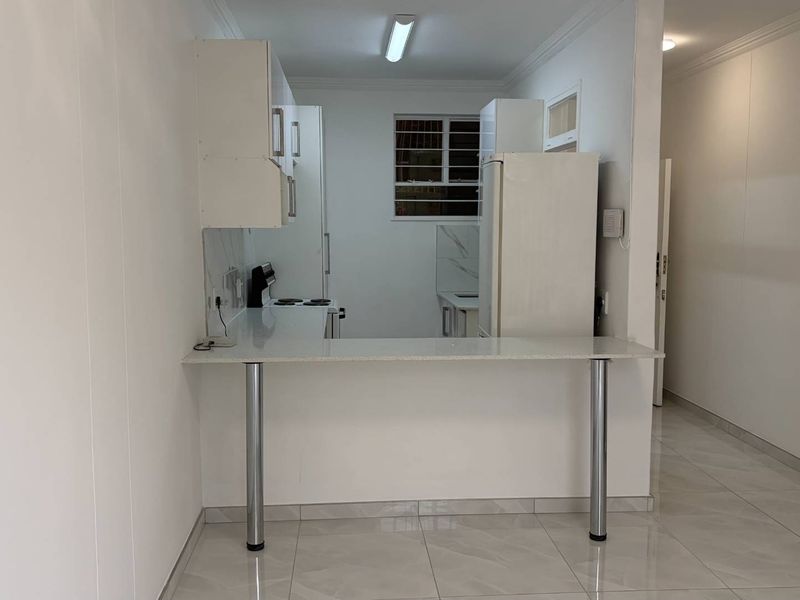 A clean, empty kitchen featuring a breakfast bar, stone countertops, built-in cabinetry, and tiled flooring, offering a bright and functional space.