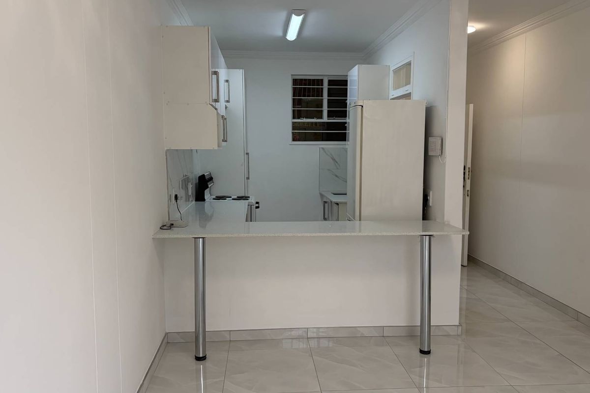 A clean, empty kitchen featuring a breakfast bar, stone countertops, built-in cabinetry, and tiled flooring, offering a bright and functional space.