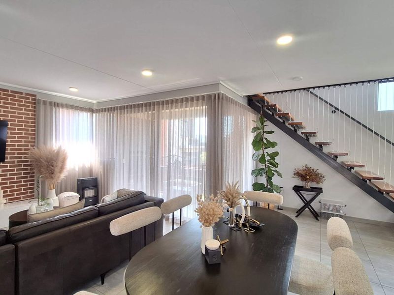 Modern open-plan living and dining area featuring an exposed brick wall, contemporary staircase with timber treads, and large sliding doors leading to the exterior.