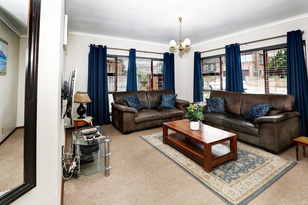 A comfortable living room featuring neutral carpeting, large windows with blinds, and a central chandelier, providing a functional and inviting space.