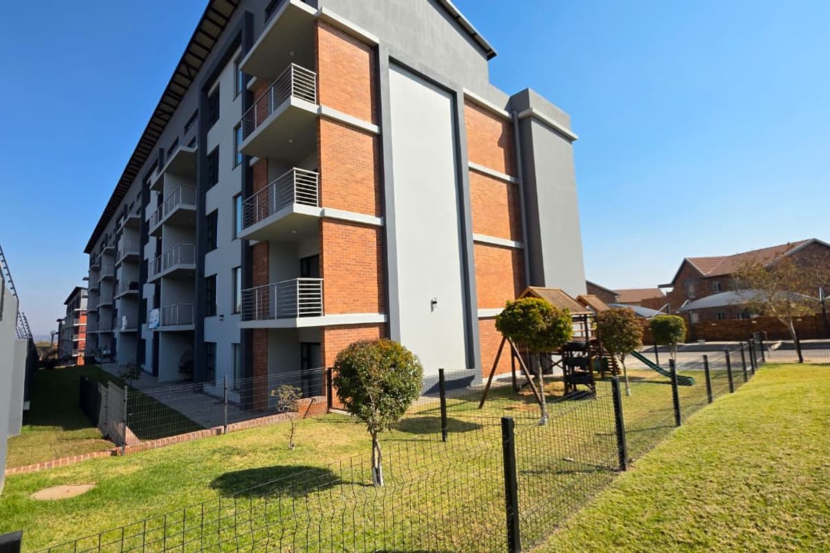 Rear view of a modern apartment complex featuring brick and plaster facade, private balconies with metal railings, and a well-maintained communal garden area.