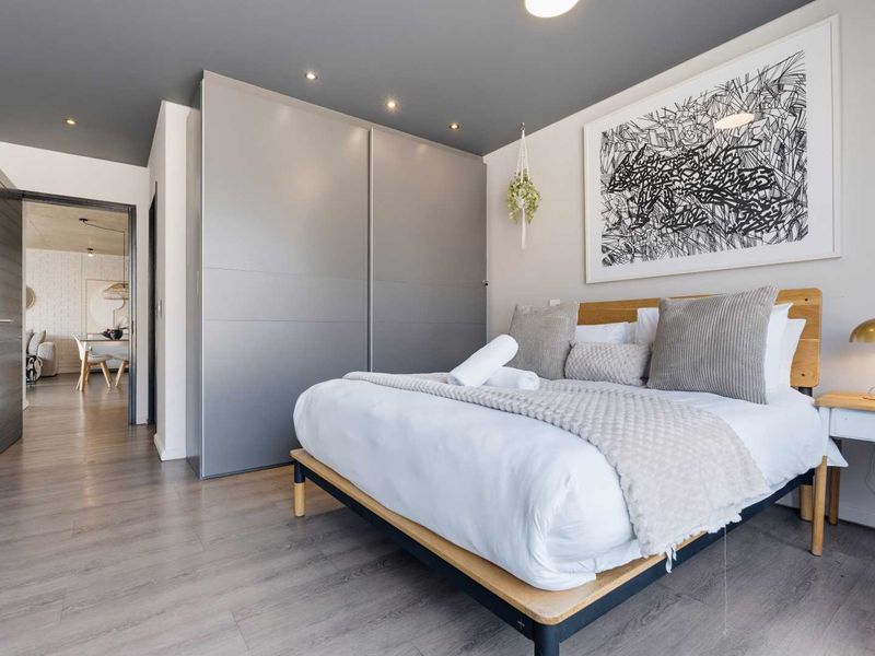Modern bedroom featuring sleek built-in wardrobes, recessed downlighting, and contemporary laminate flooring, with a view into the adjacent living area.