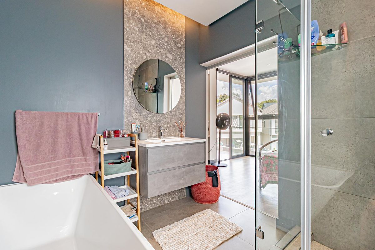 Modern bathroom featuring a floating vanity, stone-look feature wall, freestanding bathtub, and a glass-enclosed shower with contemporary finishes.