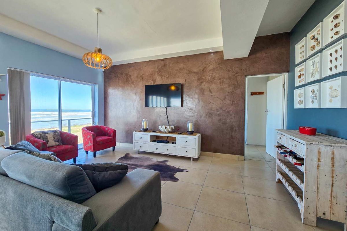 Spacious living room featuring large sliding glass doors with ocean views, tiled flooring, and a textured feature wall.