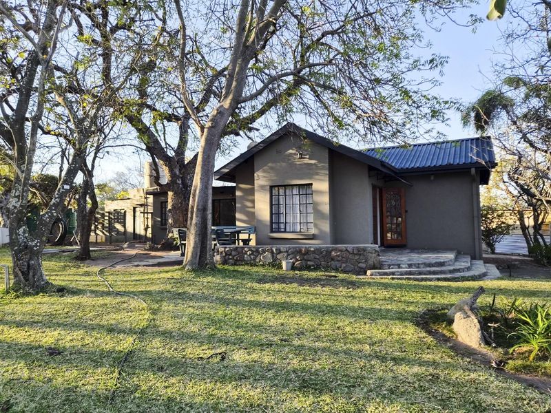 Rear view of the house featuring a stone retaining wall, paved patio area, and mature trees in the garden setting.