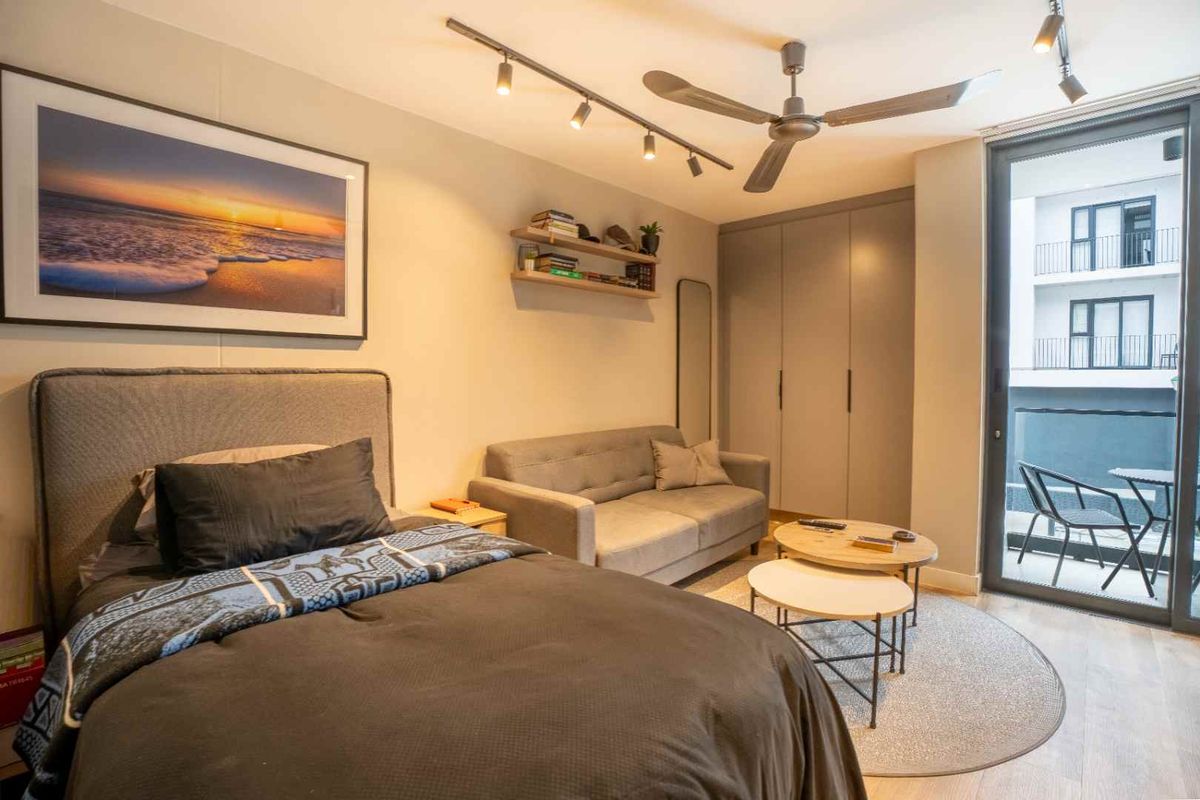 A well-maintained bedroom featuring built-in wardrobes, modern track lighting, a ceiling fan, and direct access to a private balcony through sliding glass doors.