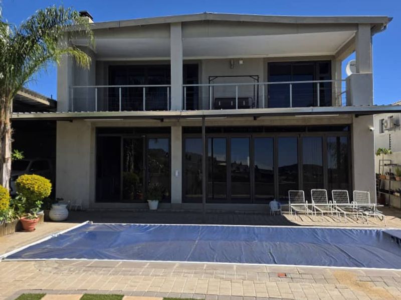 Rear view of a two-story house featuring a swimming pool with a cover, a paved patio area, and a spacious upper-level balcony.