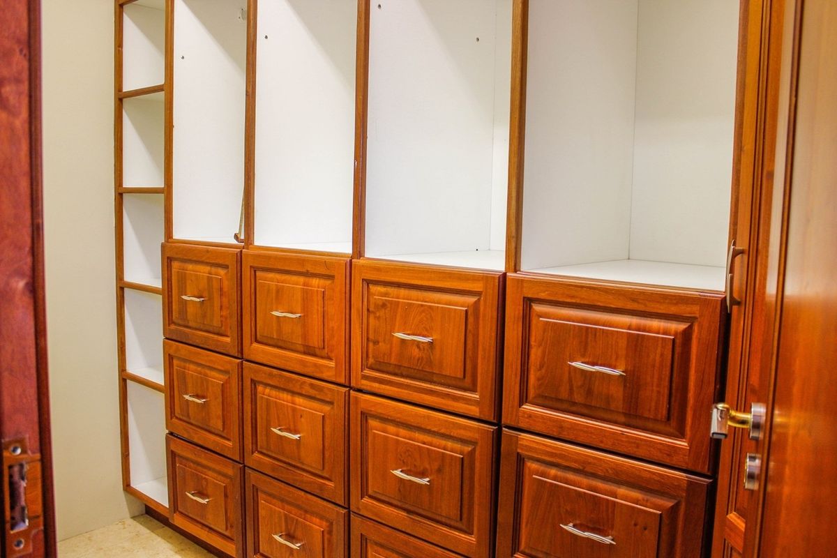 A walk-in closet or bedroom storage area featuring extensive built-in wooden cabinetry with drawers and open shelving units.