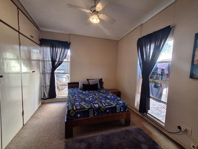 A functional bedroom featuring built-in cupboards, a ceiling fan, and carpeted flooring, providing a comfortable and practical living space.