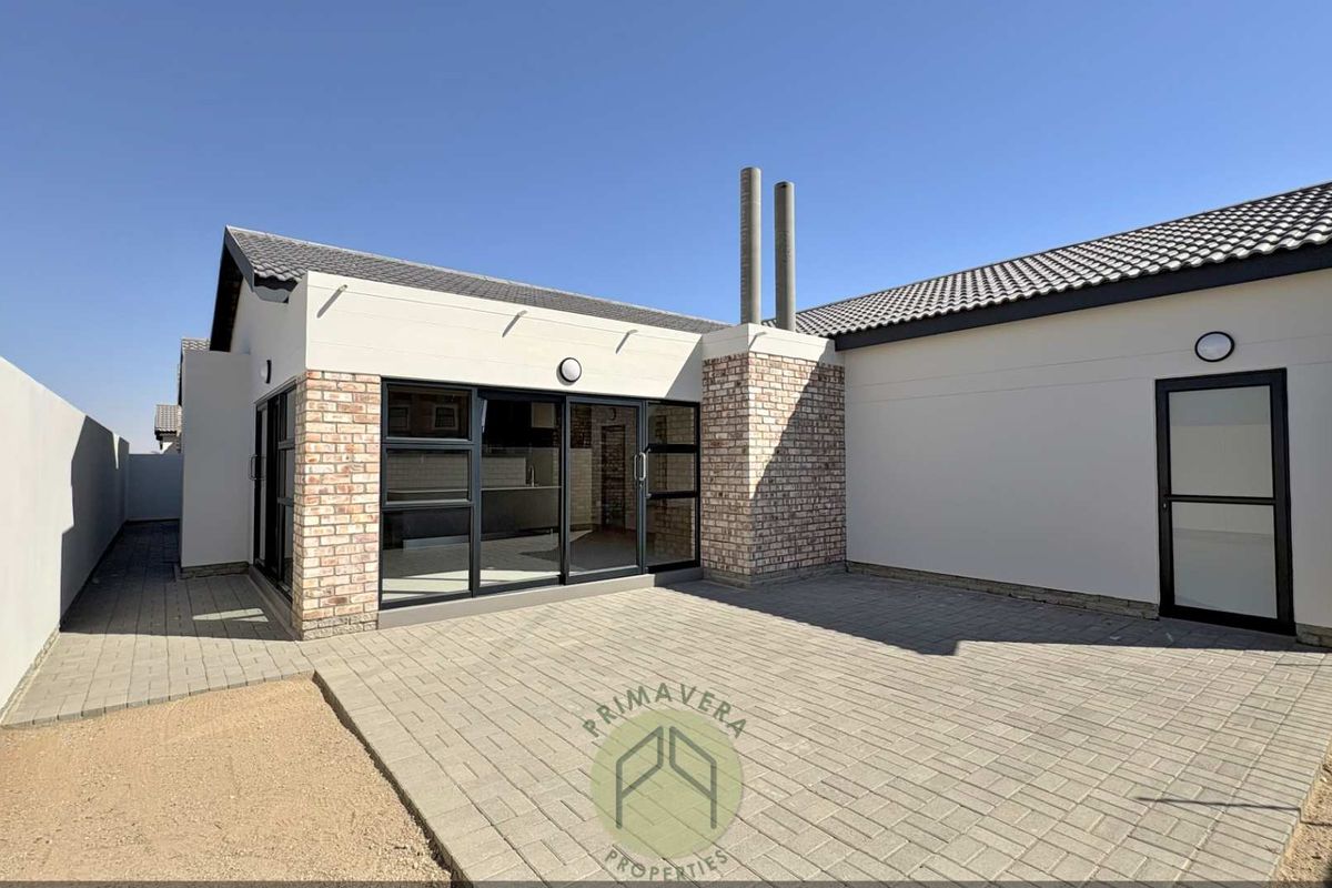A modern rear exterior view featuring a paved patio area, brick accents, and large sliding glass doors leading into the home.