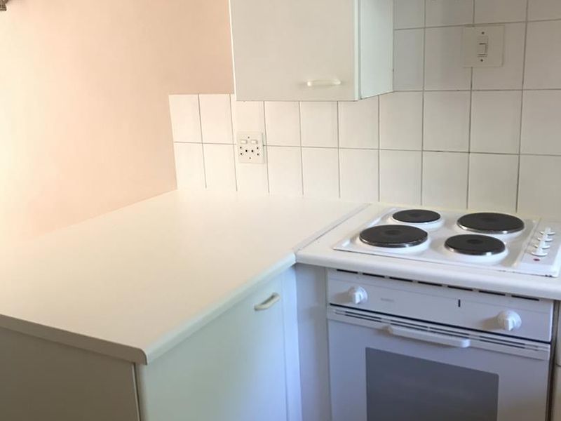A compact kitchen area featuring built-in cabinetry, a white electric stove and oven, tiled backsplash, and tiled flooring.