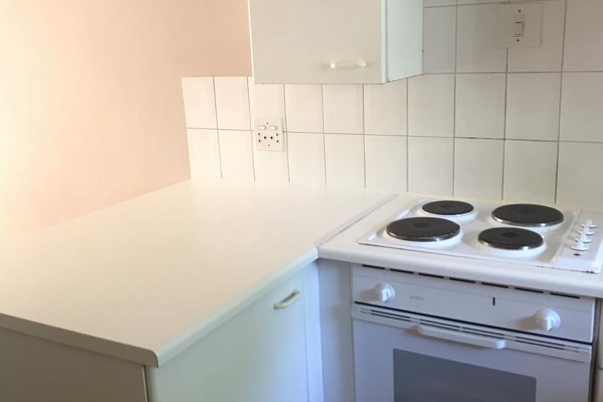 A compact kitchen area featuring built-in cabinetry, a white electric stove and oven, tiled backsplash, and tiled flooring.