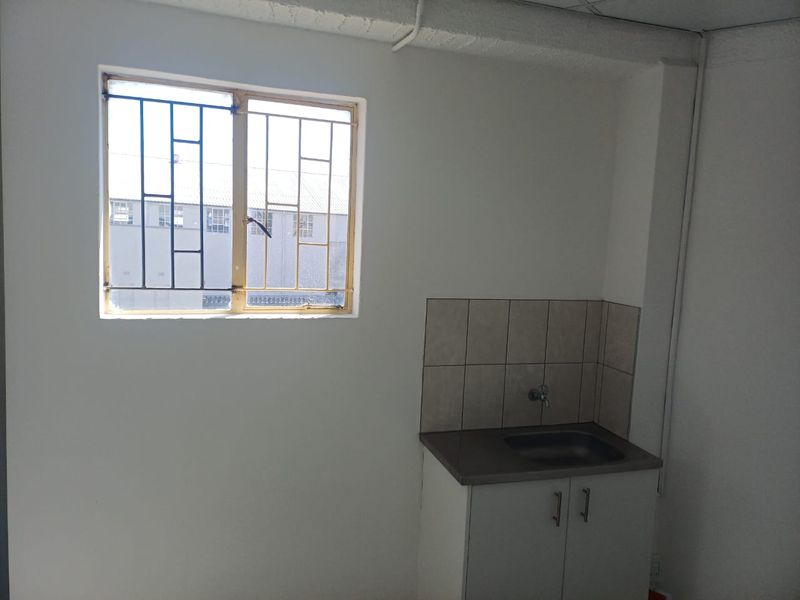 A small, functional kitchenette area featuring a built-in sink cabinet with tiled splashback and a window with security bars.