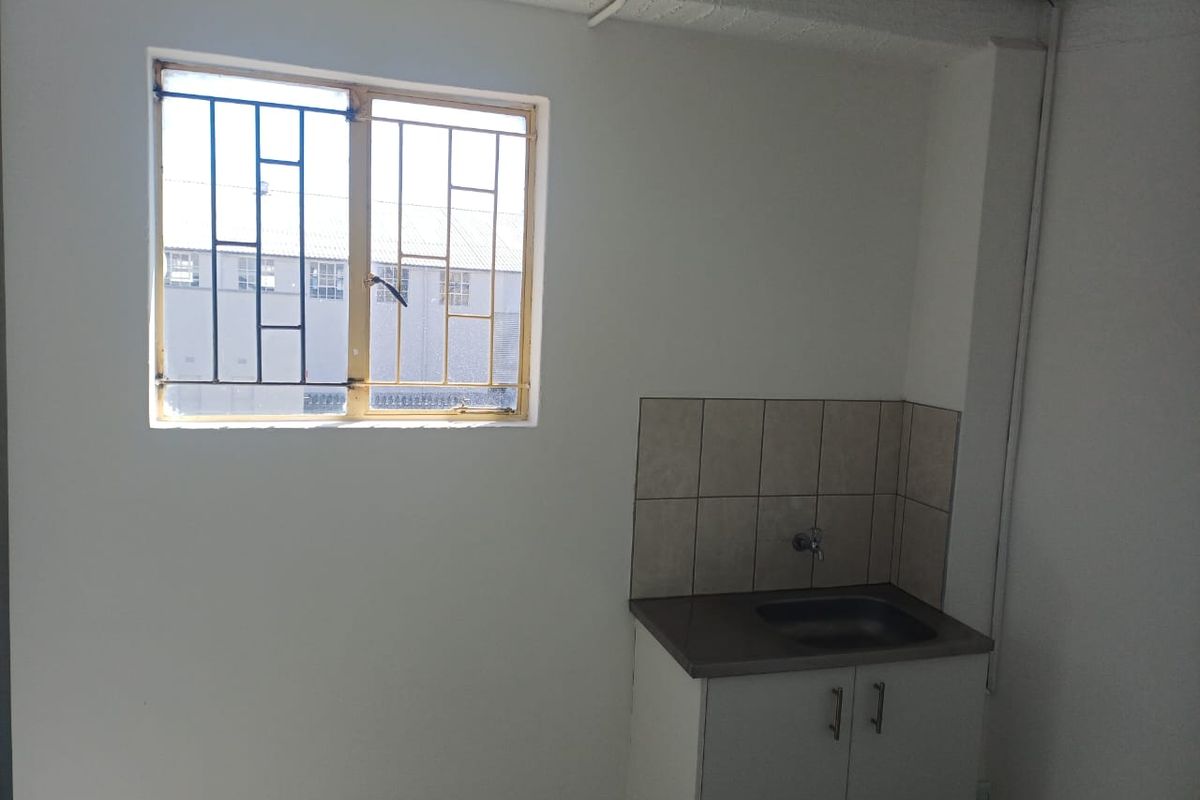 A small, functional kitchenette area featuring a built-in sink cabinet with tiled splashback and a window with security bars.