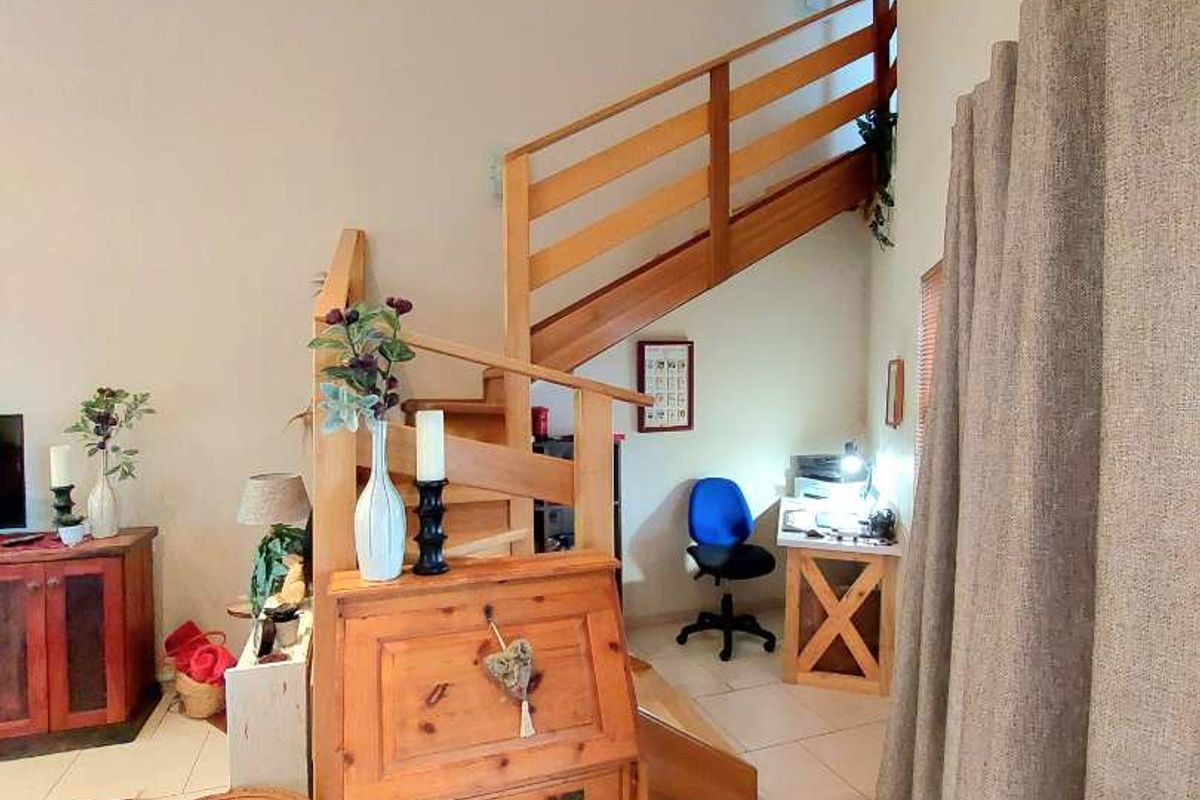 A living area featuring a wooden staircase leading to an upper level, tiled flooring, and high ceilings.