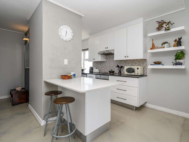 Modern kitchen featuring white cabinetry, quartz countertops, a breakfast bar, patterned tile backsplash, and polished concrete flooring.