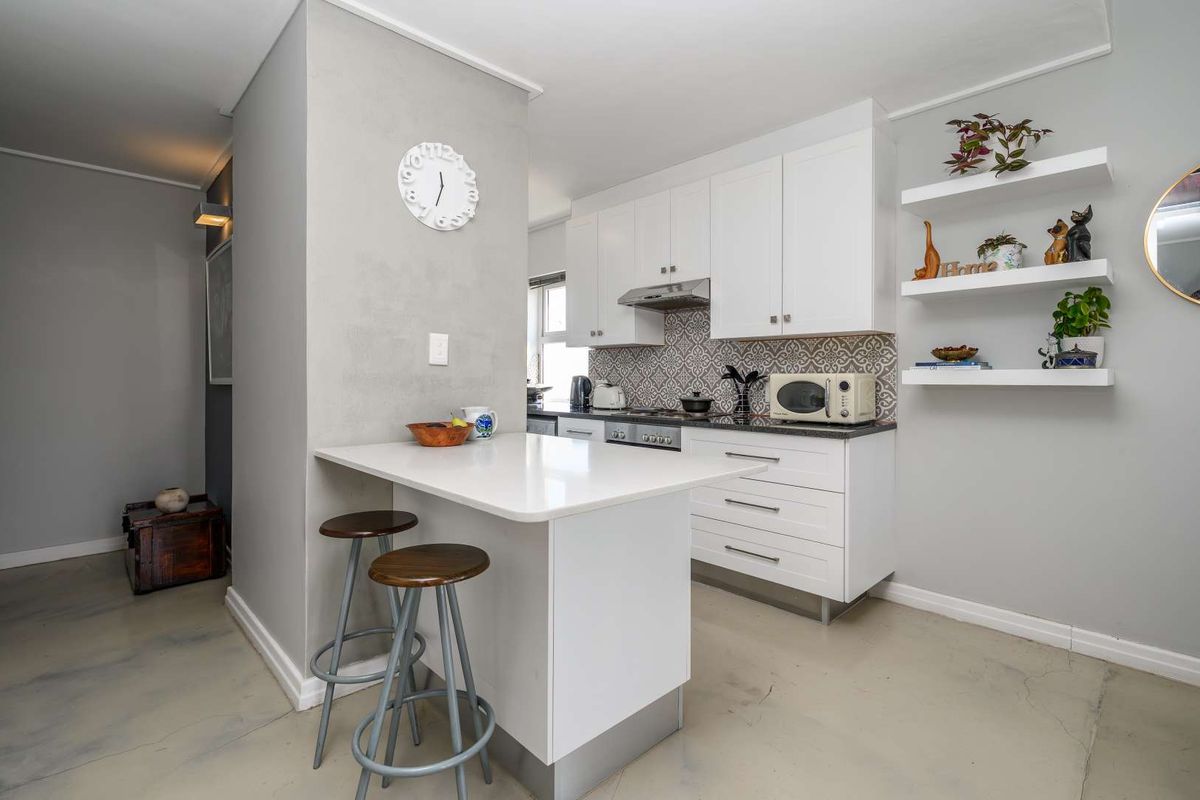 Modern kitchen featuring white cabinetry, quartz countertops, a breakfast bar, patterned tile backsplash, and polished concrete flooring.