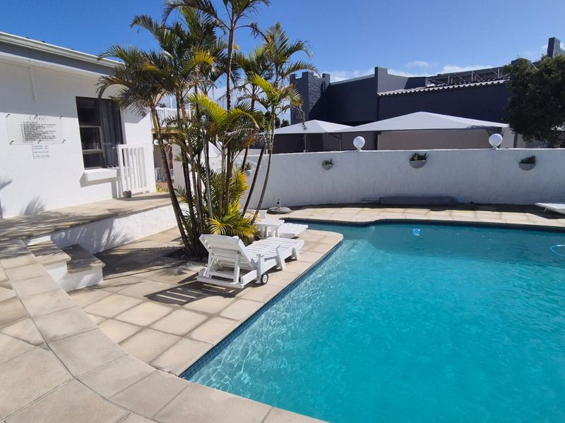 A well-maintained outdoor pool area featuring a tiled deck, boundary wall, and established landscaping, perfect for relaxation and outdoor entertainment.