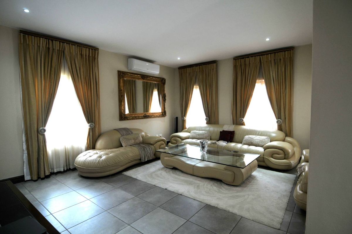 Spacious living room featuring large windows with floor-to-ceiling curtains, tiled flooring, and a wall-mounted air conditioning unit.