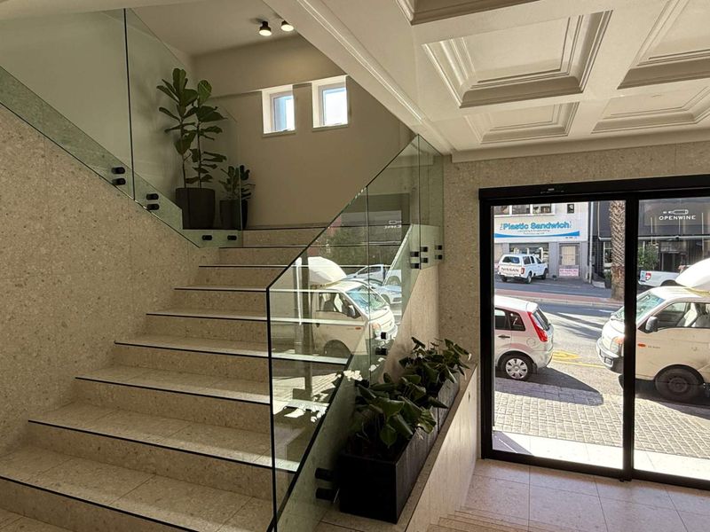 Modern office building entrance featuring a stone-clad staircase with a glass balustrade and a sophisticated coffered ceiling.