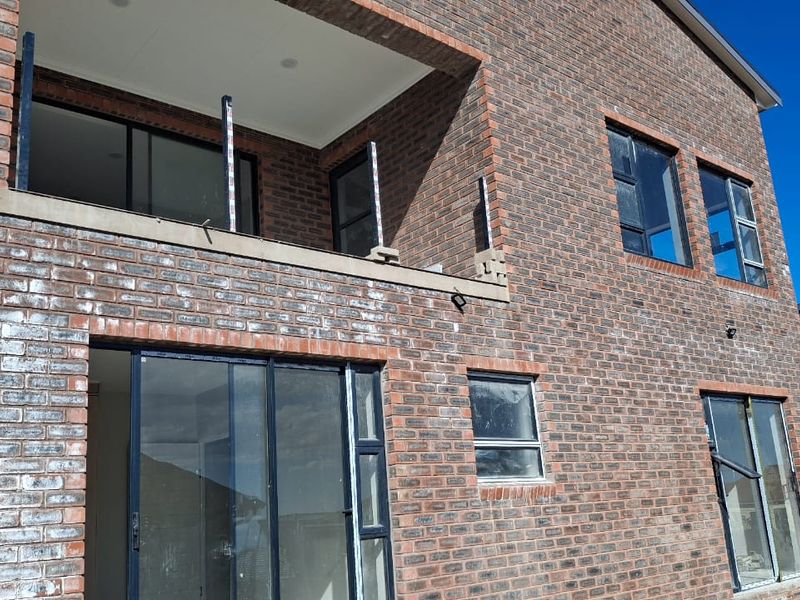 Rear elevation of a double-storey face brick house featuring aluminium sliding doors, windows, and an unfinished upper-level balcony.