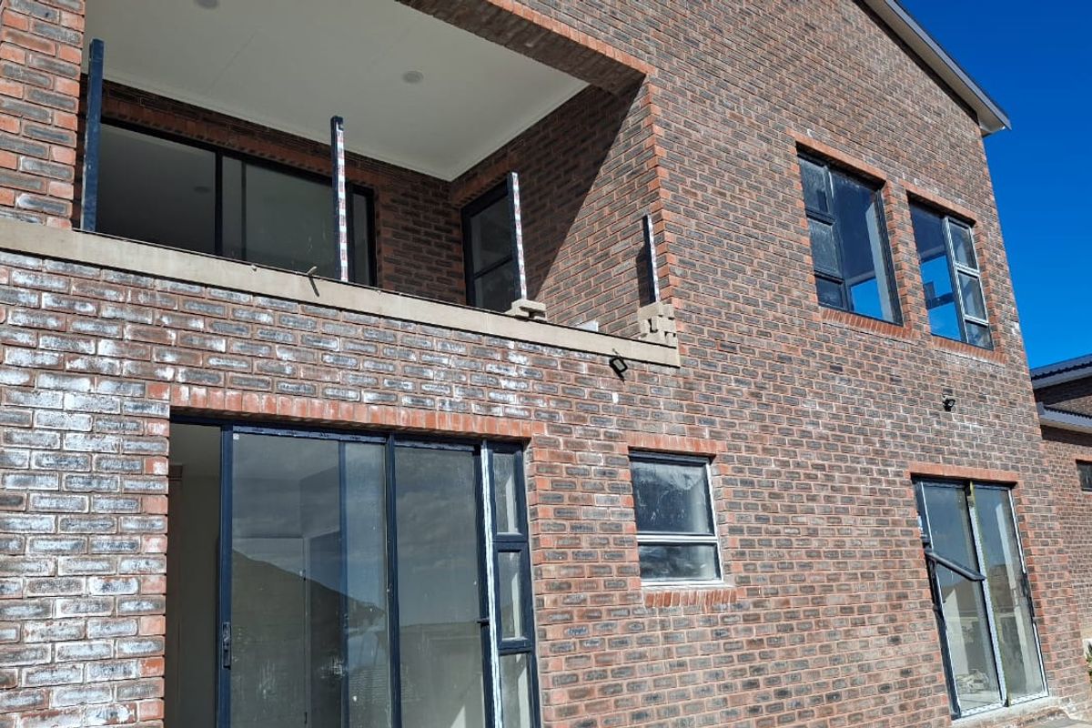 Rear elevation of a double-storey face brick house featuring aluminium sliding doors, windows, and an unfinished upper-level balcony.