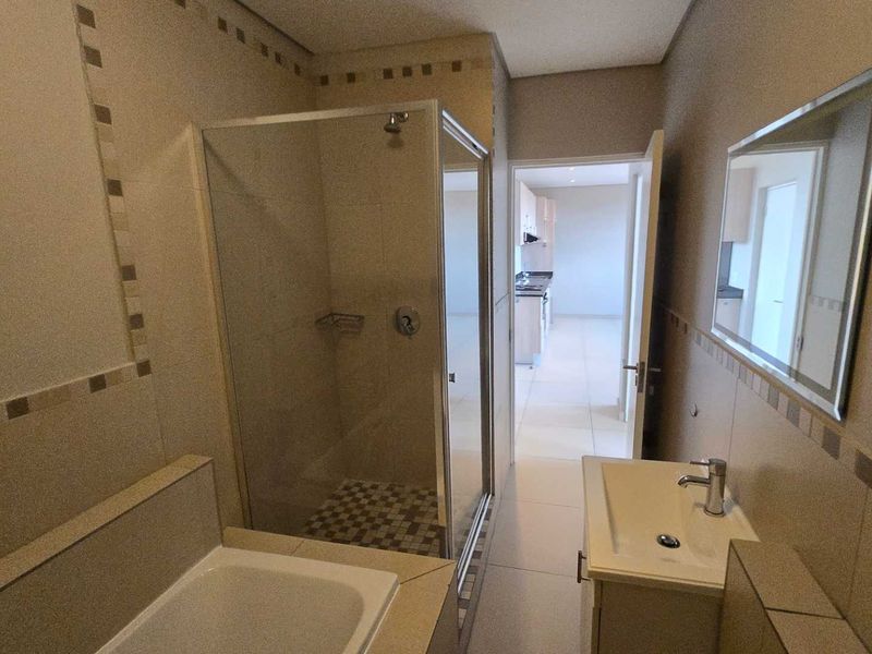 A clean, modern bathroom featuring a glass shower enclosure, a built-in bathtub, and a vanity basin with a wall-mounted mirror.